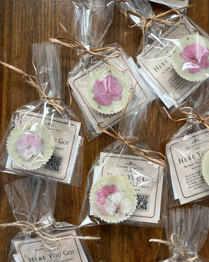 Wrapped bars of handmade soap with pressed flowers, tied with raffia and scattered across a dark walnut table.